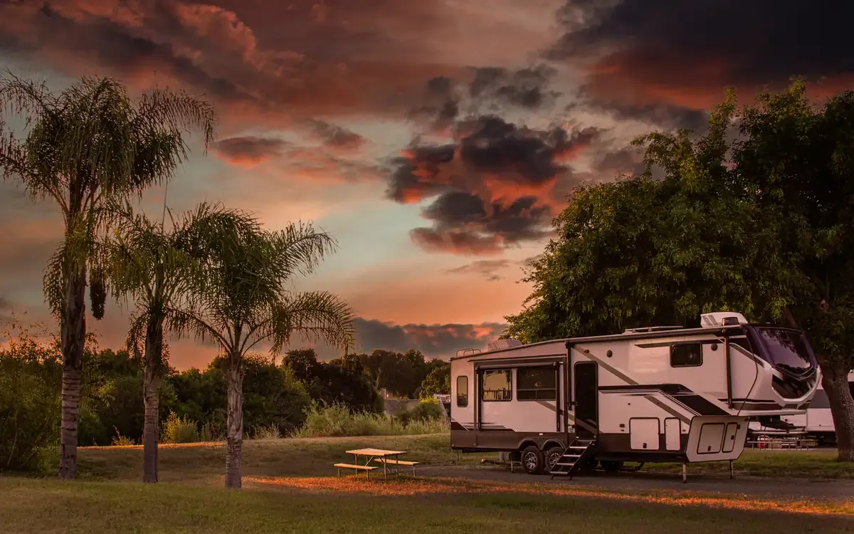 An RV camper parked next to a picnic table during a beautiful sunset.