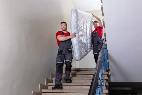 A team of movers carries a mattress down a flight of stairs.